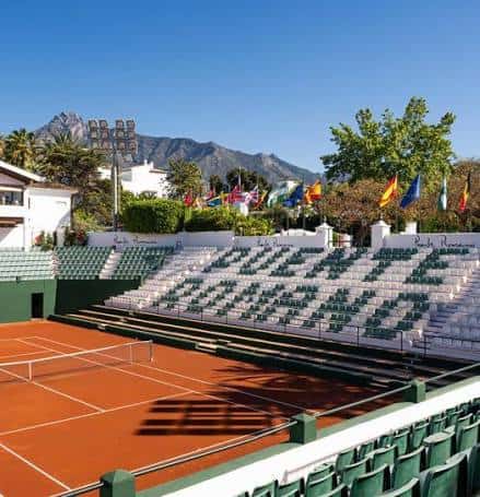 Pista central de tenis con gradas y banderas internacionales en el Puente Romano