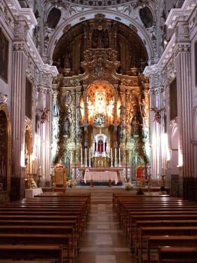 Vista interior de la nave central con el altar mayor dorado y bancos de madera