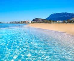 Playa de arena dorada con aguas cristalinas y montañas al fondo