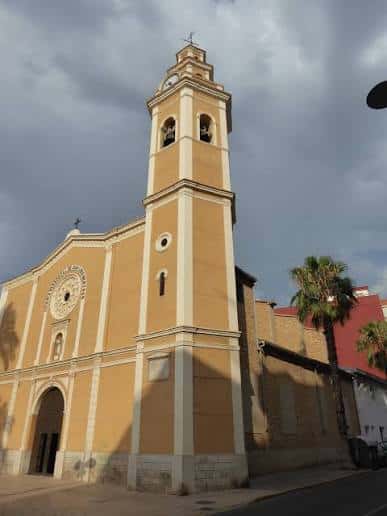 Ángulo lateral de la parroquia mostrando la torre campanario bajo cielo nublado