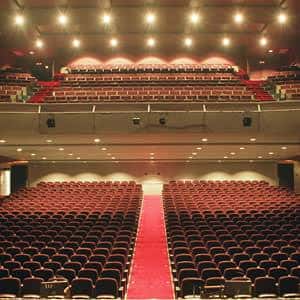 Interior del auditorio con butacas rojas, pasillo central rojo y escenario iluminado
