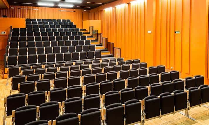 Interior del auditorio con butacas negras y paredes naranjas