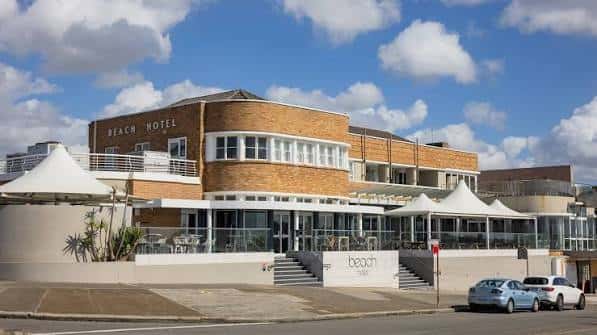 Vista exterior del Beach Hotel en Newcastle con toldos blancos y cielo azul