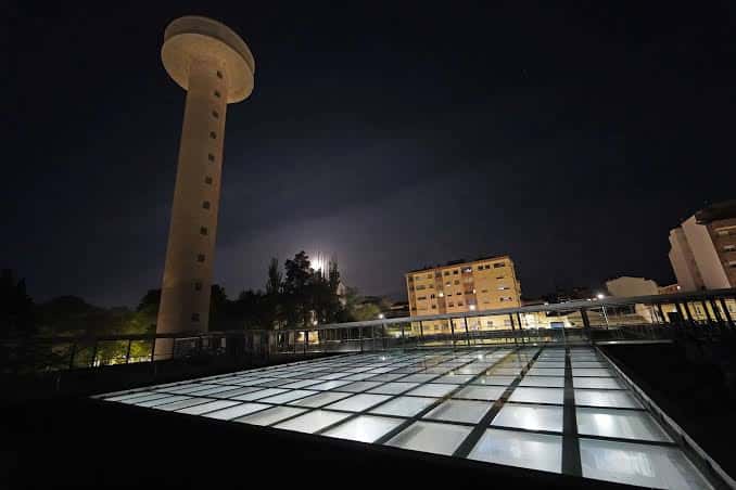 Torre del CIAb iluminada por la noche junto a una pasarela de vidrio