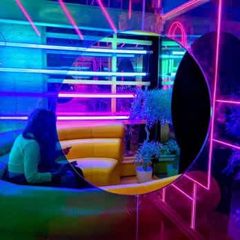 Cliente sentado en sofá amarillo frente a espejo circular con luces neón azules y rosas