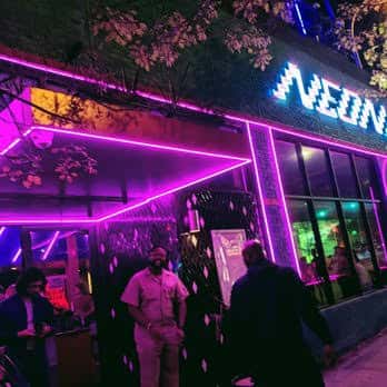 Entrada principal de Neon Grotto con letrero luminoso y personas en la acera