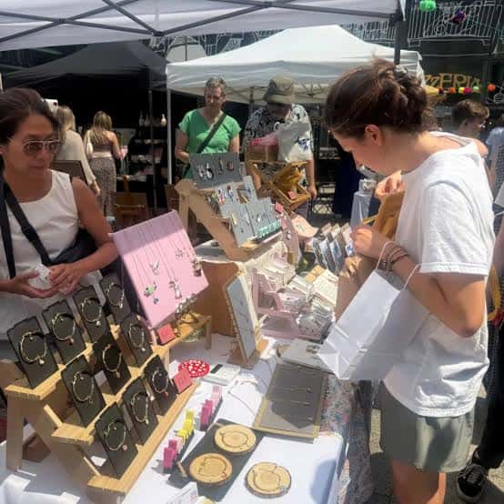 Vista de un puesto del Brighton Makers Market con joyería artesanal y clientes comprando