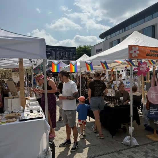 Ambiente general del mercado al aire libre con puestos bajo carpas blancas y banderas arcoíris