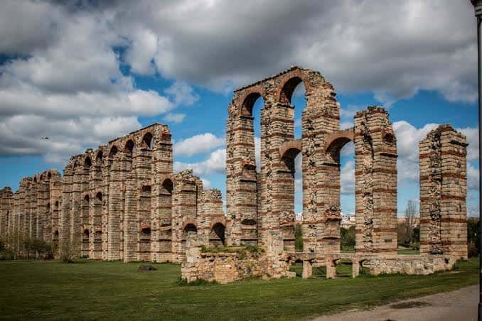 Vista panorámica del Acueducto de Los Milagros con cielo nublado y césped verde
