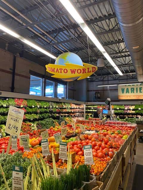 Interior vibrante de la sección de vegetales con una gran exhibición de tomates bajo letrero 'Tomato World'