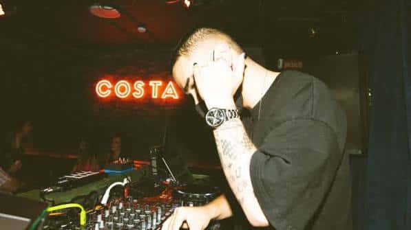 DJ actuando en el interior del Costa Social Club con neón 'COSTA' al fondo