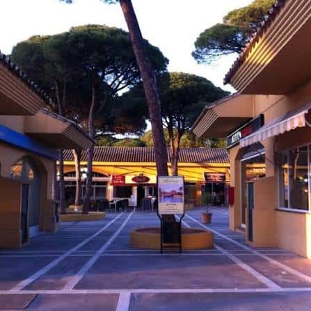 Pasillo peatonal del centro comercial con arquitectura mediterránea y árboles altos