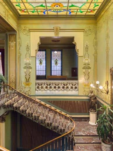 Interior del vestíbulo principal con escalera de mármol y techo de vitrales artísticos