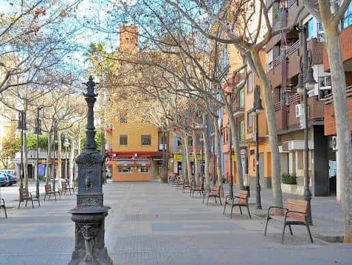 Paseo arbolado con bancos y farolas decorativas en la plaza al atardecer