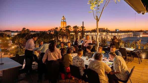 Evento social en terraza con invitados disfrutando de cena bajo luces tenues y cielo crepuscular