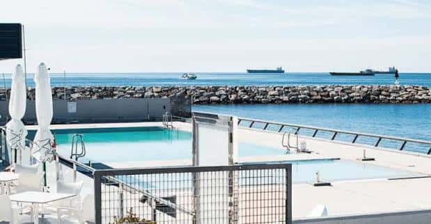 Vista de la piscina exterior del club con el mar y barcos al fondo
