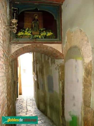 Detalle de un nicho religioso con flores sobre un arco en el carreró