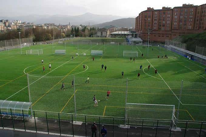 Plano aéreo de los campos deportivos con múltiples canchas y entorno urbano