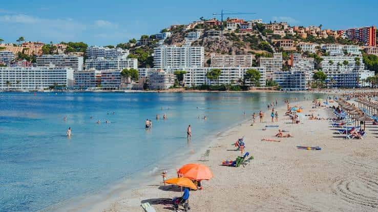 Playa con hoteles al fondo y personas disfrutando del sol