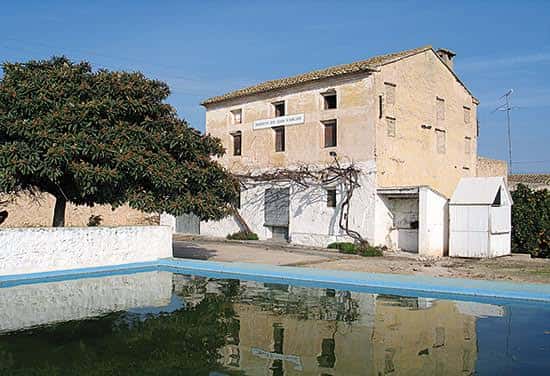 Vista exterior del edificio histórico con piscina y árboles en primer plano