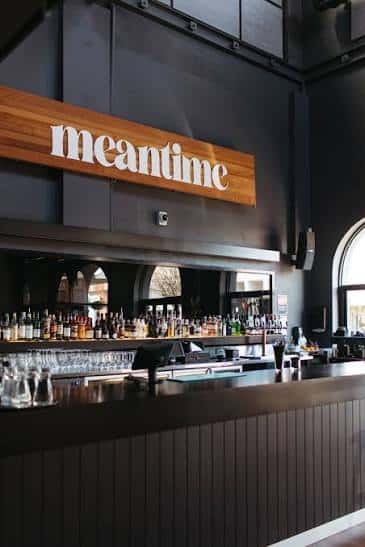 Bar principal del Meantime con estantería de botellas y letrero de madera