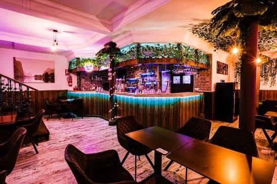 Interior del Tropicana Beach Lounge con barra iluminada en verde y decoración tropical