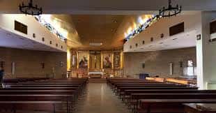 Interior de la iglesia con nave central, bancos de madera y altar principal iluminado