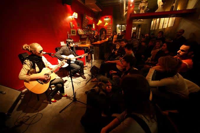 Concierto íntimo con dos músicos tocando la guitarra en un local con paredes rojas