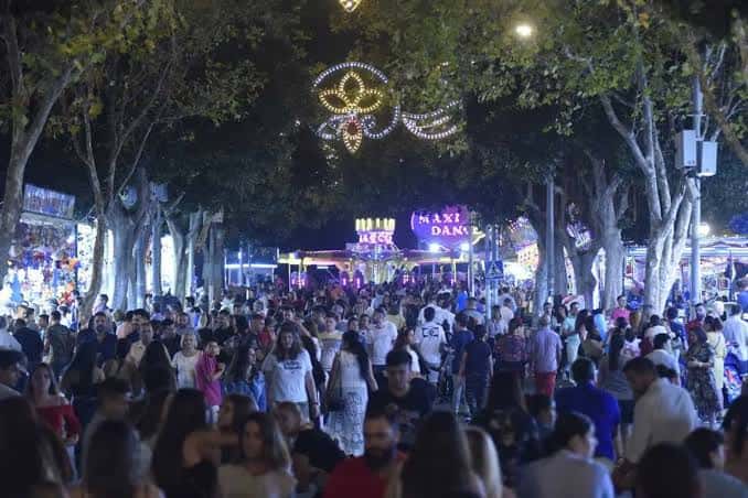 Ambiente festivo nocturno en las calles del recinto ferial con luces decorativas y multitud de visitantes