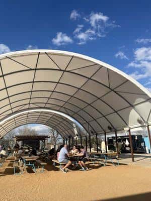 Área al aire libre bajo una estructura arqueada con mesas y personas sentadas