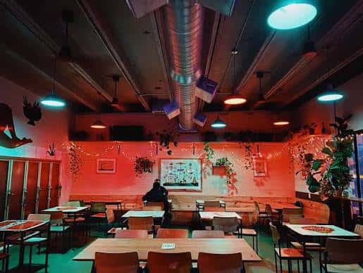 Vista nocturna del interior de Kinda Tropical con iluminación cálida y plantas decorativas