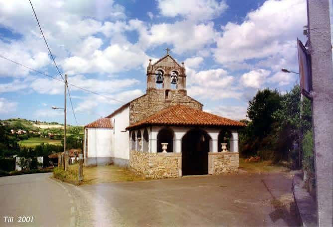 Vista exterior de la Parroquia de Caces con su característica portada y campanario bajo cielo azul