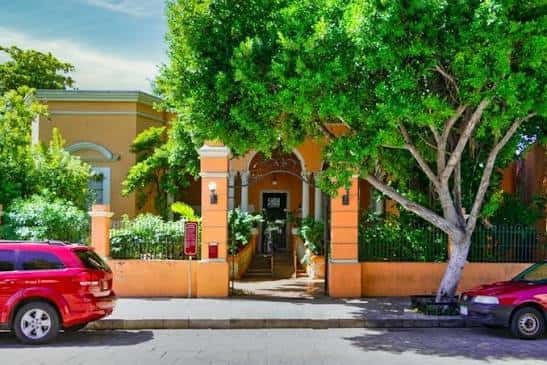 Vista frontal del museo con entrada principal, árboles frondosos y vehículos estacionados