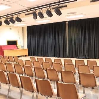 Sala de actos interior con butacas dispuestas para eventos y escenario con cortinas negras