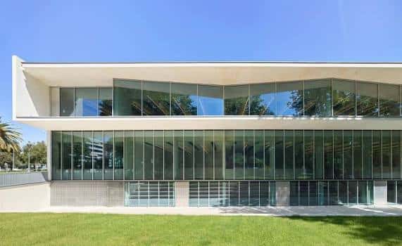 Fachada frontal de la biblioteca bajo cielo azul, destacando su diseño arquitectónico contemporáneo
