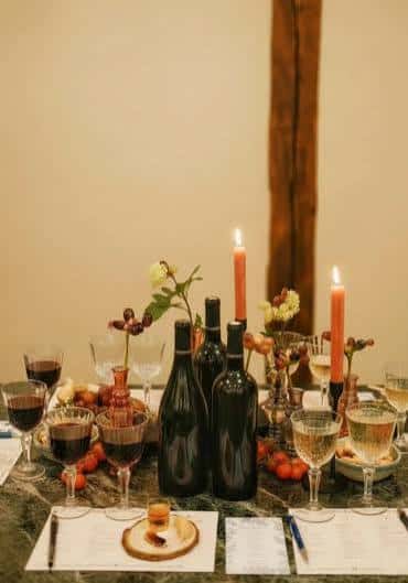 Mesa decorada para evento con velas, botellas de vino y detalles florales en La Botica de las Letras