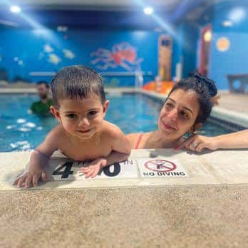 Niño sonriente apoyado en el borde de la piscina junto a una instructora en un centro de lecciones de natación