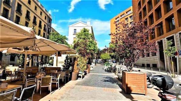 Vista soleada de la calle con mesas de restaurante y decoración urbana