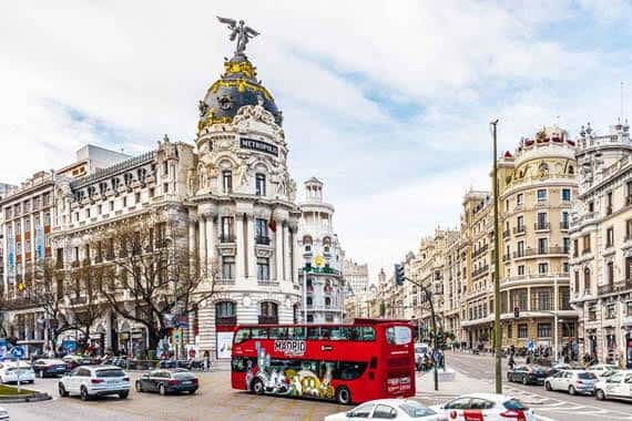 Vista panorámica de la Gran Vía con el Edificio Metrópolis y un autobús turístico rojo