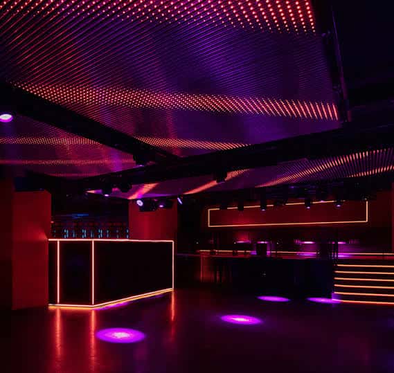 Vista del bar y zona de baile con luces neón púrpuras y techo decorativo