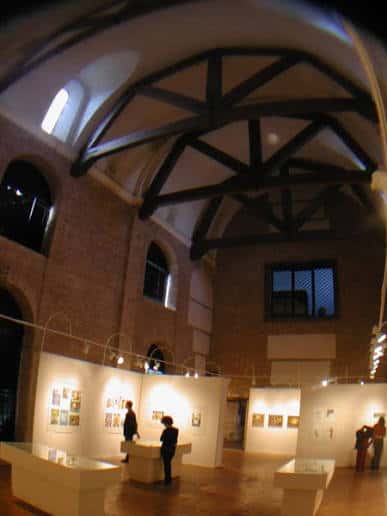 Interior del salón de exposiciones con techos de vigas de madera y paneles iluminados