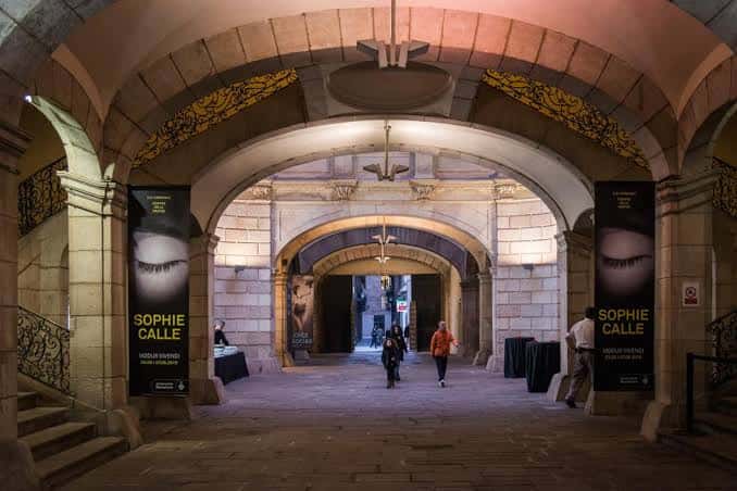 Patio interior con arcos de piedra y exposición fotográfica en banners laterales
