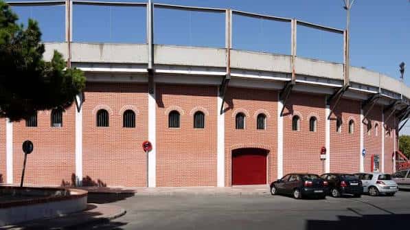 Fachada lateral de la plaza de toros con arcos y puerta roja bajo cielo despejado