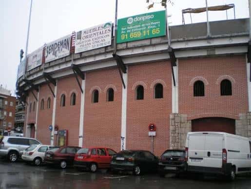Exterior de la plaza de toros con carteles publicitarios y vehículos aparcados frente a ella