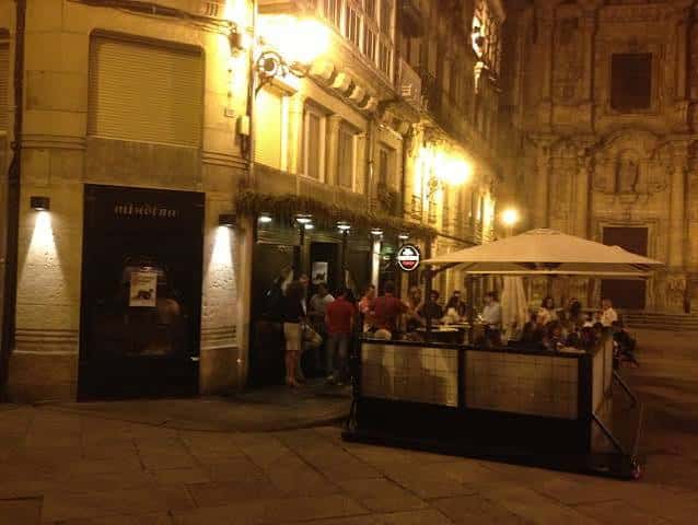 Vista nocturna de la fachada del Miudiño en Ourense con terraza iluminada y ambiente festivo