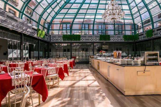 Salón de eventos con techo de cristal y mesas decoradas para celebración
