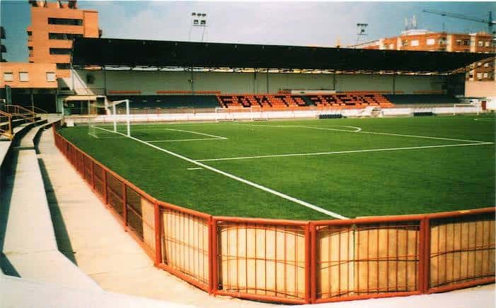 Interior del estadio mostrando la cancha verde, portería y graderío con asientos naranjas