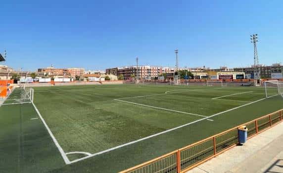 Vista panorámica del campo de fútbol con césped artificial y gradas vacías bajo un cielo despejado