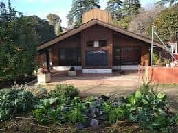 Vista frontal del Aula Ambiental La Cabaña con jardín de plantas en primer plano