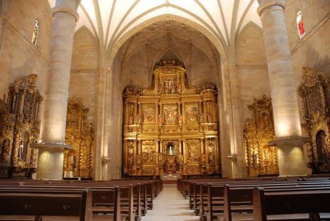 Interior de la iglesia con el retablo mayor dorado y bancos de madera